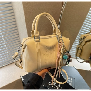 Detail of cream white Boston bag featuring 3D embossed lettering and cute doll charm