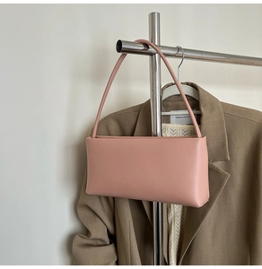Minimalist light pink leather handbag hanging on a metal stand with a blazer backdrop