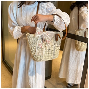 Detail of hand-woven straw tote bag with floral lace bow and brown leather handles
