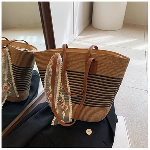 Detail of straw woven tote with black stripes and a floral lace scarf tied on the handle