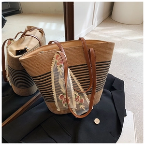 Detail view of striped woven straw tote bag with brown faux leather handles and lace scarf