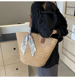 Detail of straw woven tote bag featuring brown leather handles and a blue patterned silk scarf
