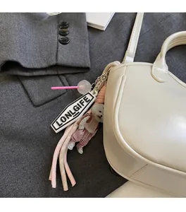 Detalle de peluche de perrito rosa y cuerda trenzada en un bolso de cuero blanco