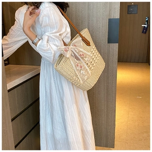 Detail of hand-woven straw tote bag with white lace ribbon bow and flower embroidery