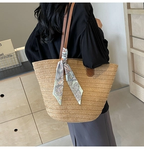 Detail of straw tote bag with brown leather strap and decorative silk scarf on shoulder