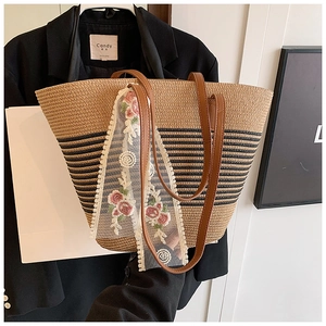 Detail of straw tote bag featuring elegant lace floral embroidery and brown leather straps