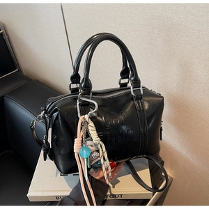 Detail of black glossy leather Boston bag with embossed text and colorful woven charm
