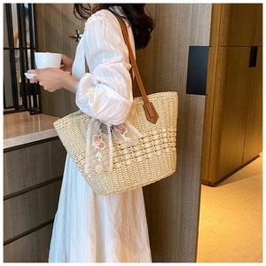 Detail of hand-woven straw tote with floral lace bow and brown leather shoulder straps