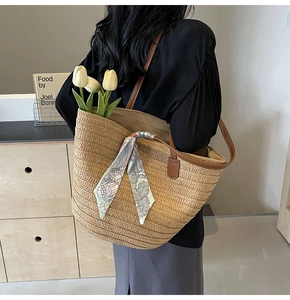 Detail of a large straw tote bag with brown leather straps and a decorative silk scarf