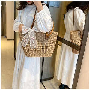 Close-up of woven straw tote bag featuring white floral lace bow and brown leather handles