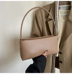 Detail of minimalist khaki leather handbag with sleek round shoulder strap held by model