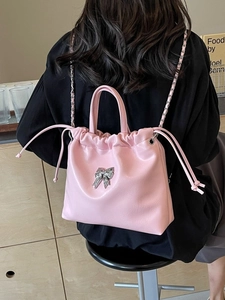 Pink drawstring chain bag with silver bow accent worn as a backpack by a model