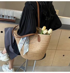 Close-up of woven straw tote bag with brown leather handles and printed silk scarf detail