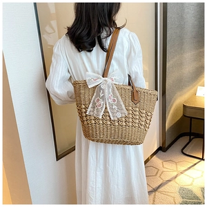 Detail of handwoven straw tote bag with lace bow and floral embroidery on strap