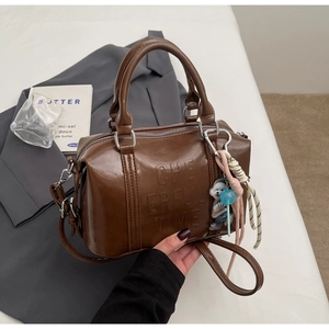 Close-up of brown leather Boston bag with embossed text and bear charm accessory