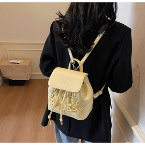 Detail view of cream-colored backpack with pearl accents and embossed letters on a model