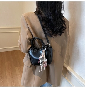 Detalle de bolso negro brillante con colgante de cachorrito y etiqueta en un traje