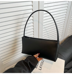 Close-up of minimalist black rectangle shoulder bag with elegant slim handle and matte leather texture