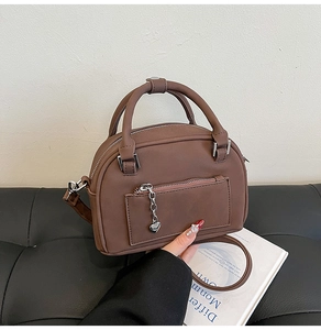 Dettaglio borsa a bauletto in pelle opaca marrone scuro con ciondolo a cuore e tracolla