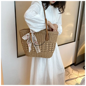Detail of large woven straw tote bag with brown leather straps and floral lace ribbon