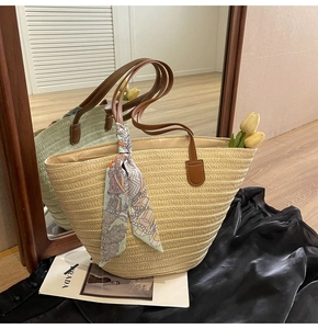 Detail of straw tote bag featuring brown leather handles and a decorative silk scarf