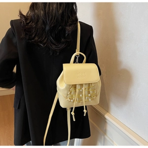 Detail of yellow mini backpack featuring pearl woven decor and embossed logo flap