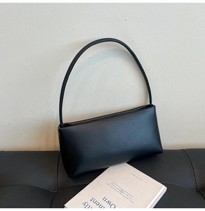 Minimalist black baguette bag made of matte faux leather resting on a leather bench