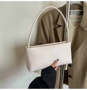 Minimalist cream leather underarm bag held by a model wearing a brown blazer
