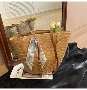 Detail of a large woven straw tote bag with brown leather handles and a colorful silk scarf