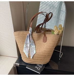 Detail of straw woven tote bag featuring brown handles and a decorative blue floral scarf