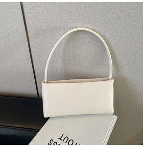 Detail of minimalist cream rectangular handbag with slim handle on a book display