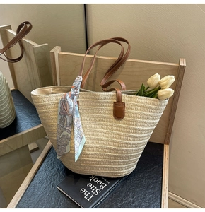 Detail of woven straw tote bag featuring brown leather straps and floral silk scarf