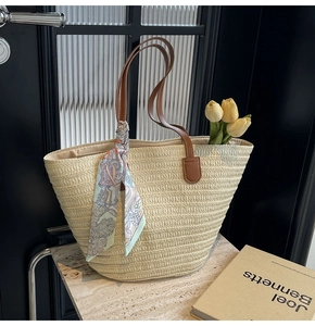 Detail of straw tote bag with brown leather straps and geometric patterned scarf