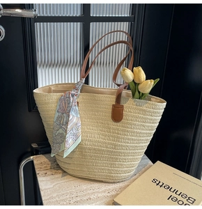 Detail view of woven straw tote bag with brown leather handles and a silk scarf accent