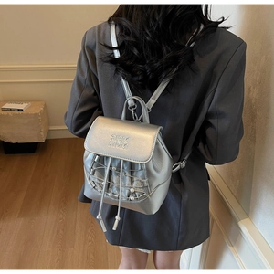 Detail of silver mini backpack with MM logo engraving and pearl drawstrings on grey blazer