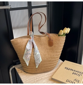 Detail of woven straw tote bag featuring leather handles and a floral silk scarf accent