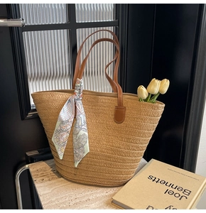 Detail of straw woven tote bag featuring brown leather handles and a geometric silk scarf