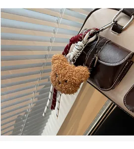 Close-up of a brown teddy bear plush charm with woven rope on a stylish shoulder bag