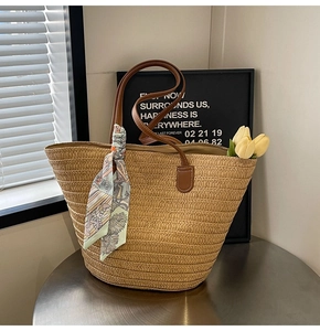 Detail of hand-woven straw tote with brown leather handles and decorative floral scarf