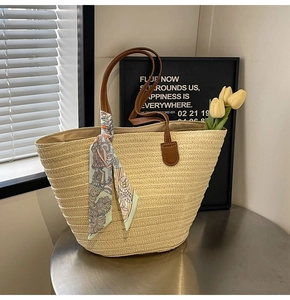 Close-up of woven straw tote bag featuring brown leather straps and horse print silk scarf