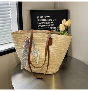 Detailed straw tote bag with brown leather straps and vintage print scarf on metal table