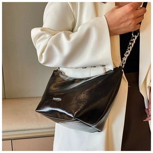 Detail of black glossy shoulder bag with silver metal chain strap and logo plaque