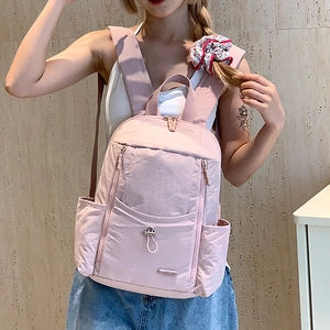 Detail of light pink nylon backpack featuring multi-pocket storage and drawstring buckle