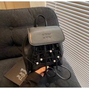 Detail view of a black mini leather backpack featuring white pearls and grid lacing detail
