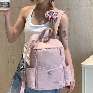 Detailed view of pink nylon backpack with multi-pocket design on model's back