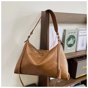 Detail of a brown leather hobo bag hanging on a wooden bookshelf in a cozy room