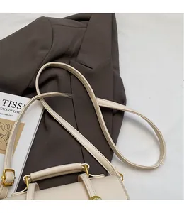 Detail of a creamy white leather crossbody bag with gold hardware and top handle