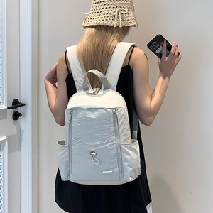 Detailed back view of a light beige nylon travel backpack with multiple pockets on a model