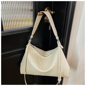 Creamy beige leather hobo bag with wide shoulder strap hanging on a black door handle