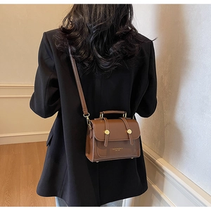 Close-up of retro brown messenger bag with gold hardware on a black blazer